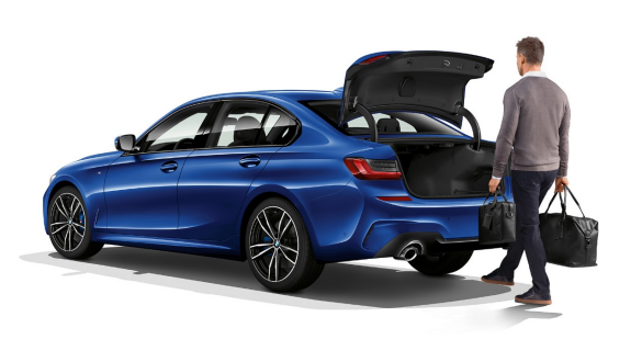 Deschidere şi închidere fără atingere a hayonului BMW Seria 3 Sedan. Imagine cu trei sferturi din partea spate a BMW Seria 3 Sedan staţionând, în timp ce conducătorul auto deschide automat hayonul cu piciorul.Deschidere şi închidere fără atingere a hayonului BMW Seria 3 Sedan.