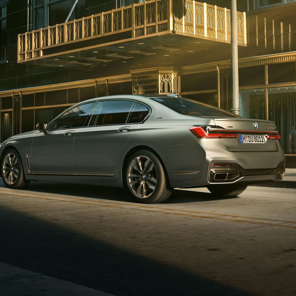 BMW M760Li xDrive cu motor V12 Perspectivă laterală din spate asupra BMW M760Li xDrive staţionând în faţa unor zgîrie-nori într-un peisaj urban