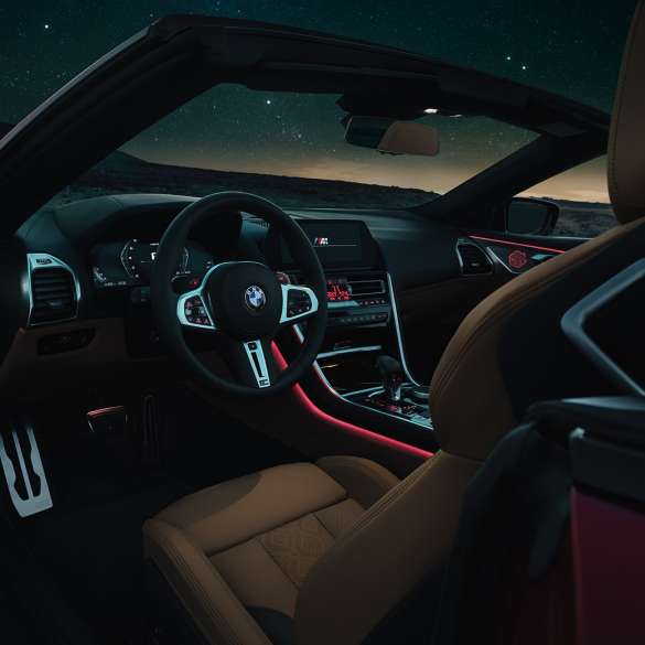 Habitaclul BMW M8 Competition Cabriolet. Habitaclul BMW M8 Cabriolet cu volan sport îmbrăcat în piele şi iluminare ambientală roşie, pe timp de noapte.