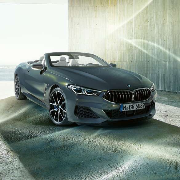 Imagine cu trei sferturi din partea frontală a BMW M850i xDrive Cabriolet. Imagine cu trei sferturi din partea frontală a BMW M850i xDrive Cabriolet în Gri Dravit metalizat cu soft-top-ul deschis, staţionând în faţa coastei.
