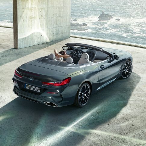 Perspectivă de sus asupra BMW M850i xDrive Cabriolet. Perspectivă de sus asupra BMW M850i xDrive Cabriolet în Gri Dravit metalizat cu soft-top-ul deschis, parcând într-o parcare de beton în faţa oceanului.