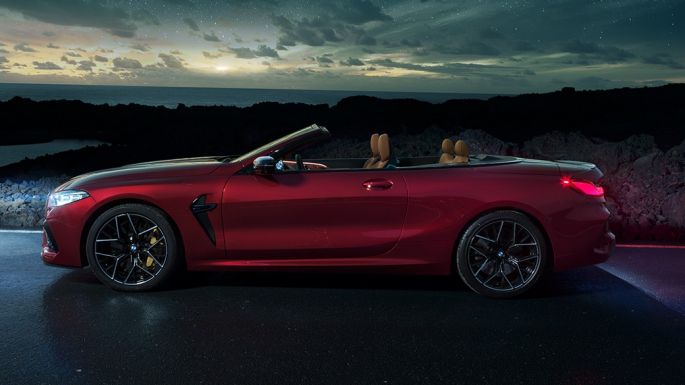 Imagine cu partea laterală a BMW M8 Competition Cabriolet. Imagine cu partea laterală a BMW M8 Competition Cabriolet în Roşu Motegi metalizat cu soft-top-ul deschis, staţionând noaptea sub cerul înstelat.