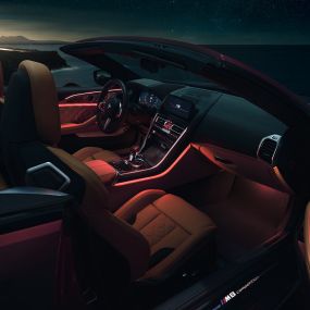 Interiorul BMW M8 Competition Cabriolet. BMW M8 Competition Cabriolet cu soft-top-ul deschis şi interior cu iluminare ambientală roşie, pe timp de noapte.