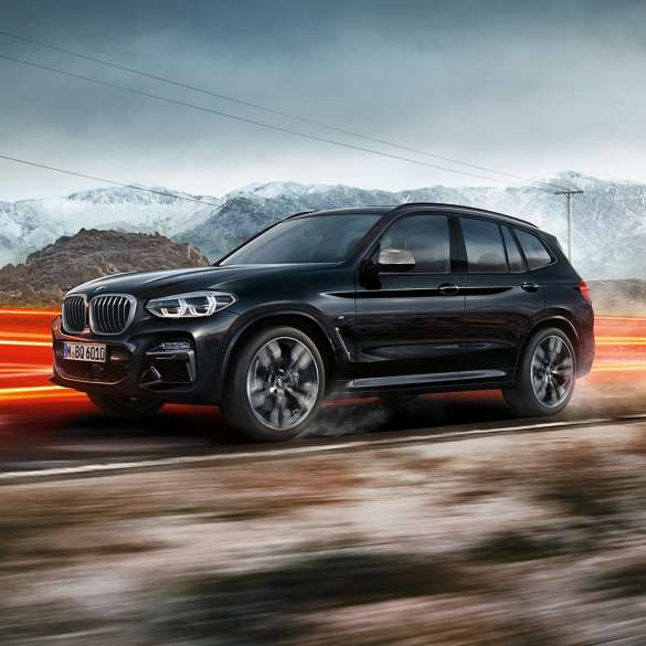Perspectivă laterală a BMW X3 M40i şi BMW X3 M40d. Perspectivă laterală a exteriorului BMW X3 M40i şi BMW X3 M40d în Negru Sapphire metalizat rulând într-un peisaj montan cu raze de lumină.