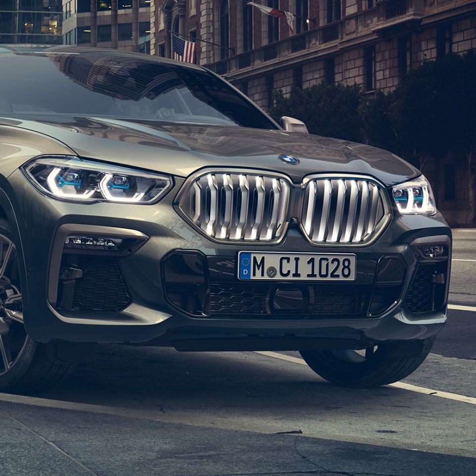 BMW X6 M50i staţionând Imagine cu trei sferturi din perspectivă frontală a BMW X6 M50i, staţionând în faţa unui peisaj urban