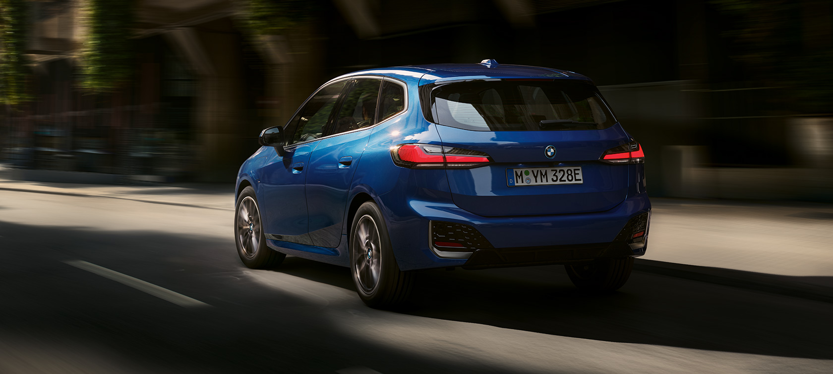 BMW Seria 2 Active Tourer 230e plug-in hybrid deplasându-se prin oraş Imagine din partea din spate a BMW Seria 2 Active Tourer 230e plug-in hybrid, în Albastru Portimao M, deplasându-se prin oraş