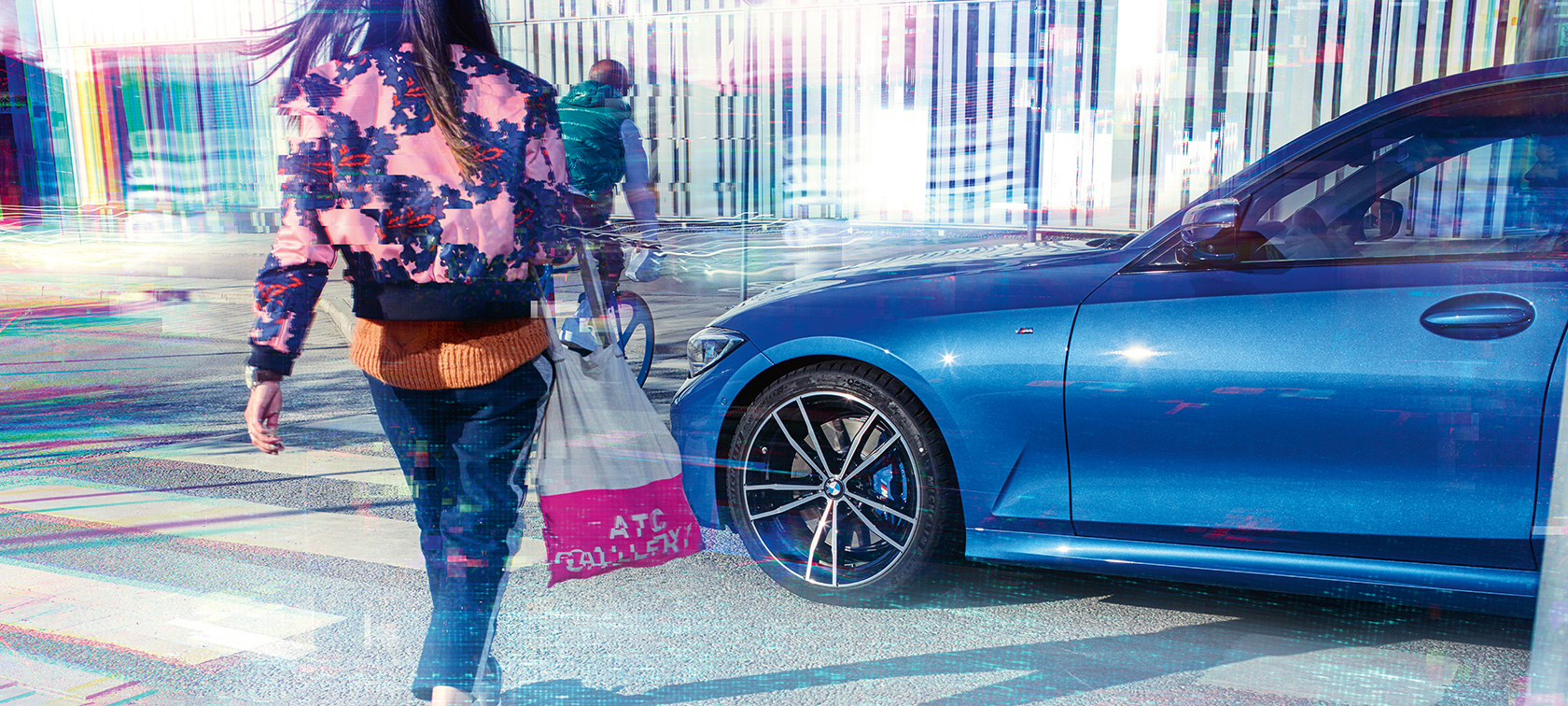Imagine cu trei sferturi din partea laterală a BMW Seria 3 Sedan. Imagine cu trei sferturi din partea laterală a BMW Seria 3 Sedan cu pasageri, aflat pe şosea în faţa unui fundal urban.