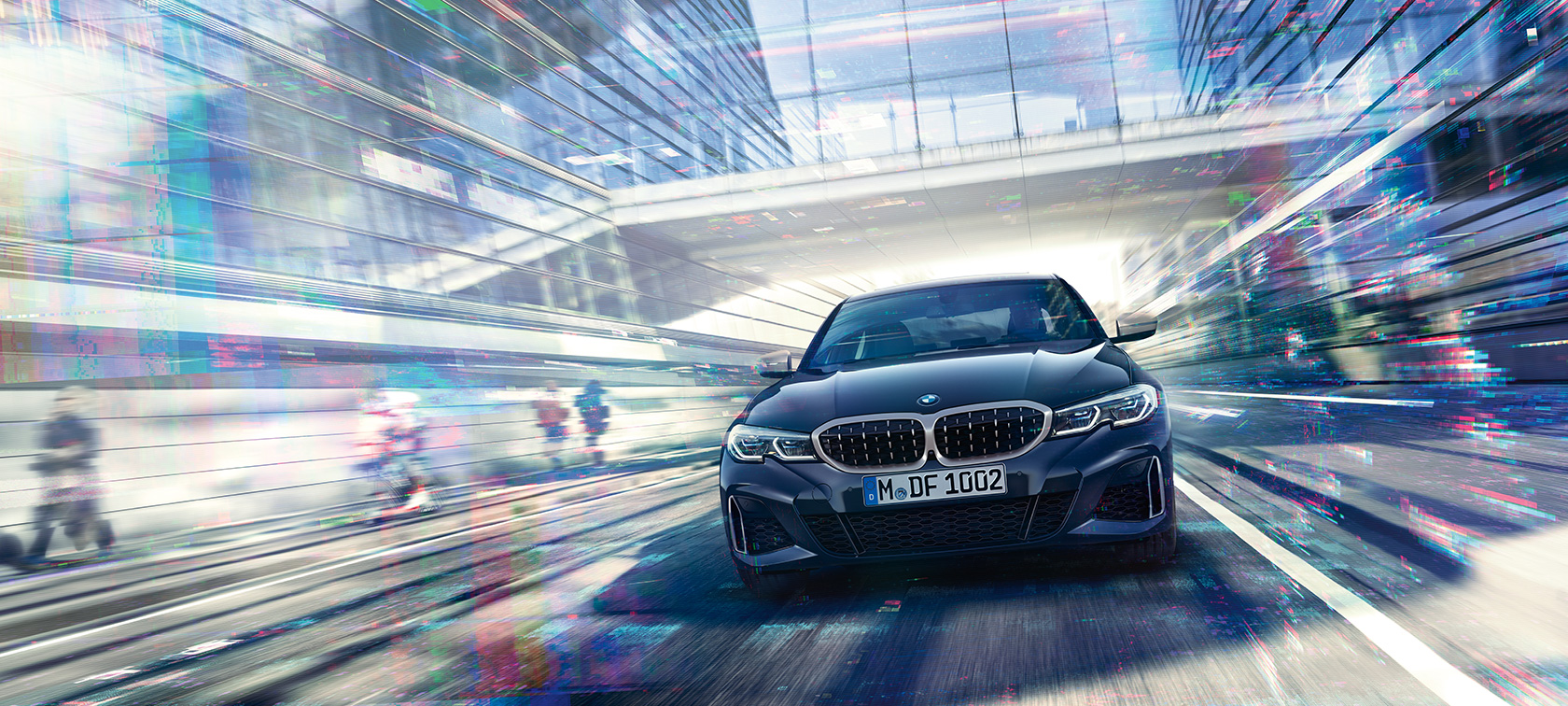 Imagine frontală cu BMW M340i xDrive Sedan al BMW Seria 3. Imagine frontală cu BMW M340i xDrive Sedan în oraş printre clădiri din sticlă.