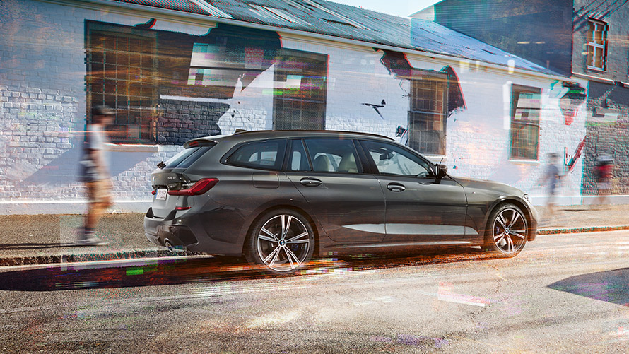 BMW Seria 3 Touring (G21), Gri Dravit, 7/8 imagine din partea din spate BMW Seria 3 Touring (G21), Gri Dravit, 7/8, imagine din partea din spate, în faţa unei clădiri