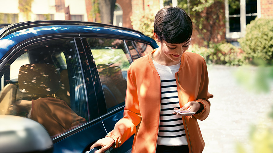 BMW Service Femeie cu un smartphone lângă portiera modelului său BMW BMW Service Femeie cu un smartphone lângă portiera modelului său BMW