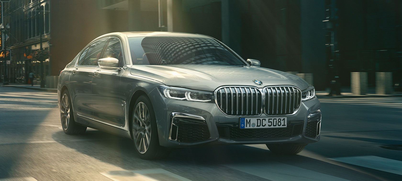 Imagine cu trei sferturi din partea frontală a BMW Seria 7 Sedan gri Imagine cu trei sferturi din partea frontală a BMW Seria 7 Sedan gri rulând într-un peisaj urban