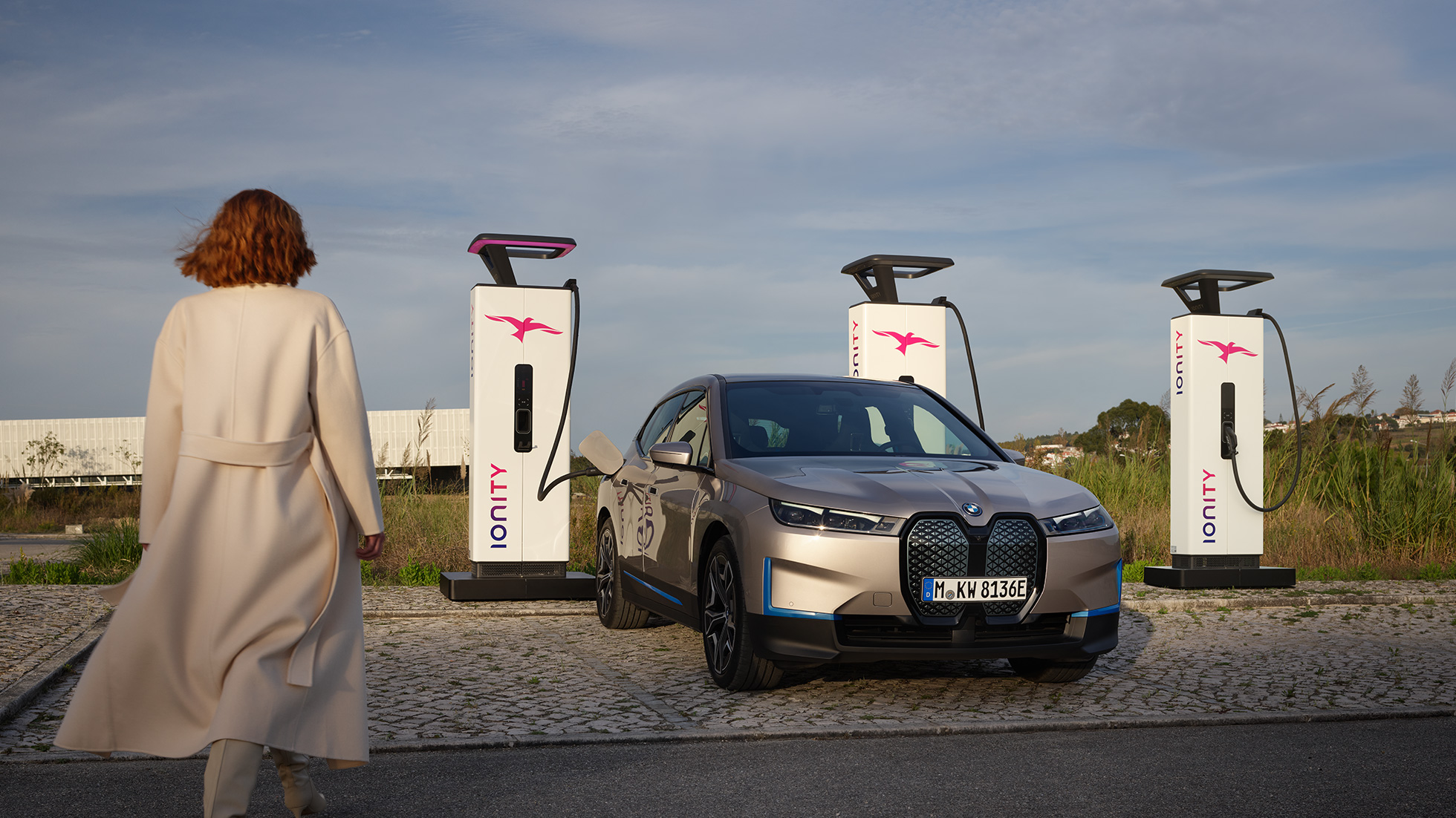 Imagine cu trei sferturi din partea frontală a BMW iX, la staţie de încărcare Imagine cu trei sferturi din partea frontală a BMW iX 20, Argintiu Cashmere, la staţie de încărcare