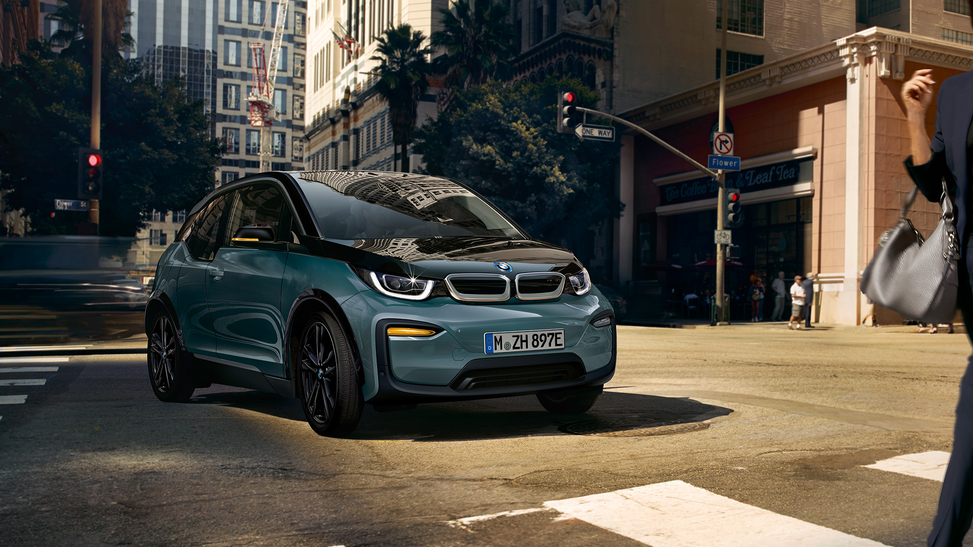 Imagine cu trei sferturi din partea frontală a BMW i3, 2018, rulând Imagine cu trei sferturi din partea frontală a BMW i3, I01, 2018, în Bej Jucaro cu detalii în Gri Frozen metalizat, rulând într-un spaţiu urban