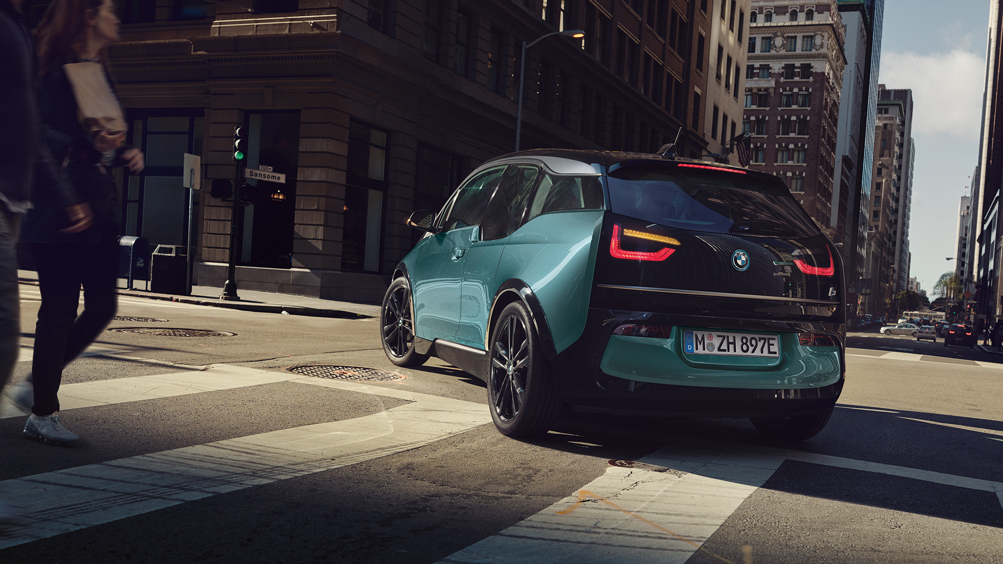 Imagine cu trei sferturi din partea spate a BMW i3, 2018, rulând Imagine cu trei sferturi din partea spate a BMW i3, I01, 2018, în Bej Jucaro cu detalii în Gri Frozen metalizat, rulând într-un peisaj urban