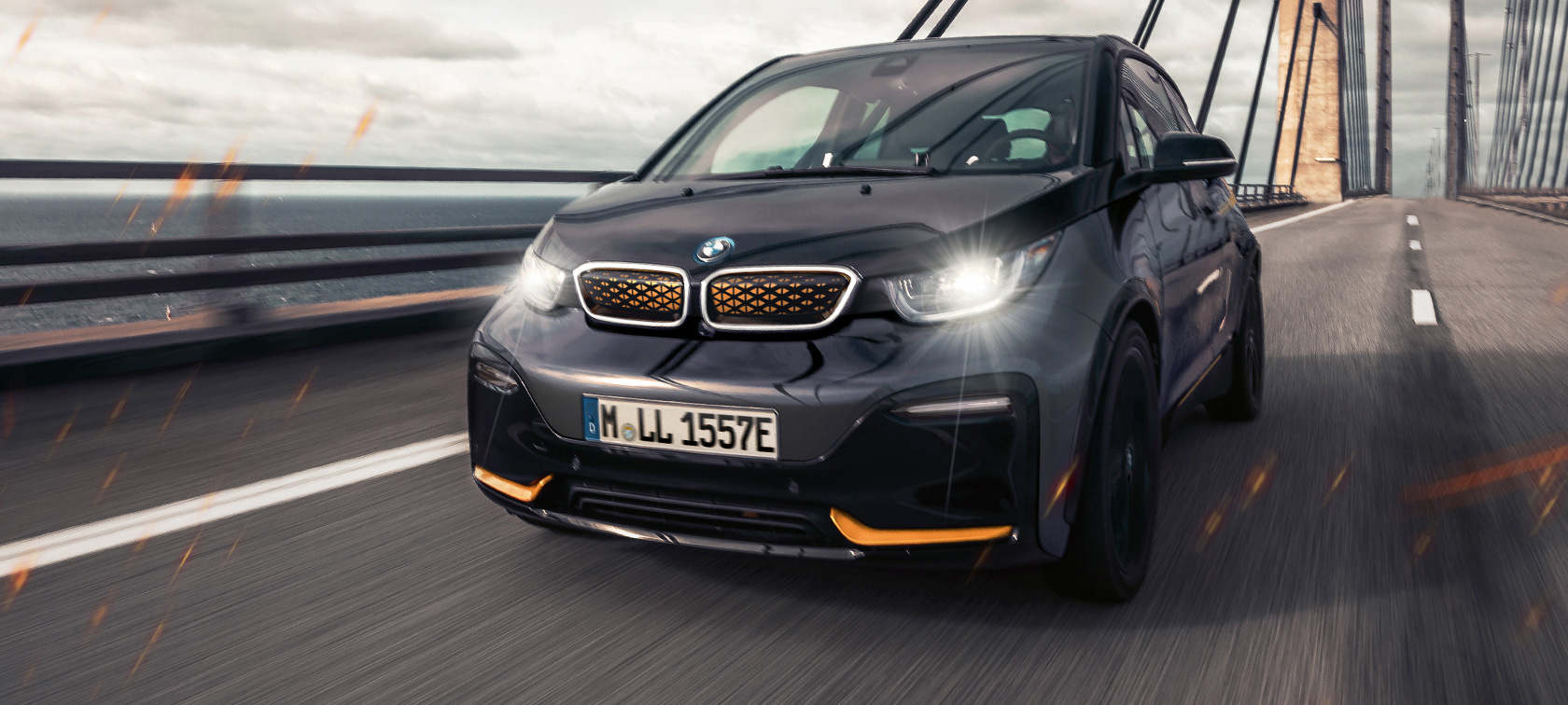 Imagine cu trei sferturi din partea frontală a BMW i3 I01 Ediţia Unique Forever Imagine cu trei sferturi din partea frontală a BMW i3 I01 Ediţia Unique Forever în Storm Bay cu accent Frozen E-Copper, rulând pe autostradă
