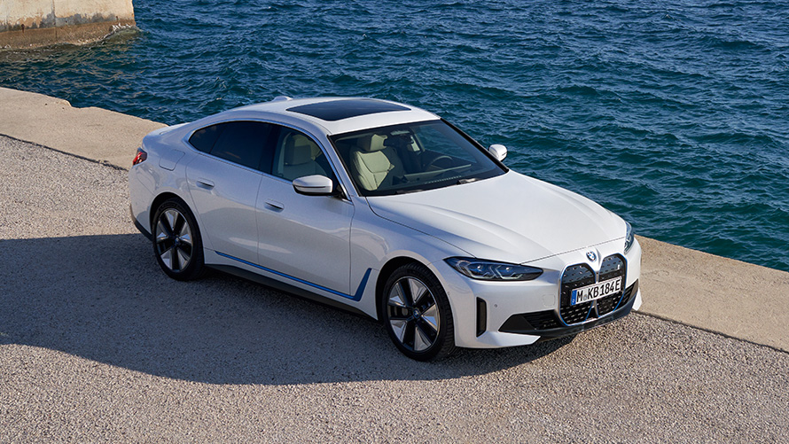 Imagine cu trei sferturi din partea frontală a unui BMW i4 eDrive40 G26 2021 care staţionează lângă un chei Imagine cu trei sferturi din partea frontală a unui BMW i4 eDrive40 G26 2021 Alb Mineral care staţionează lângă un chei