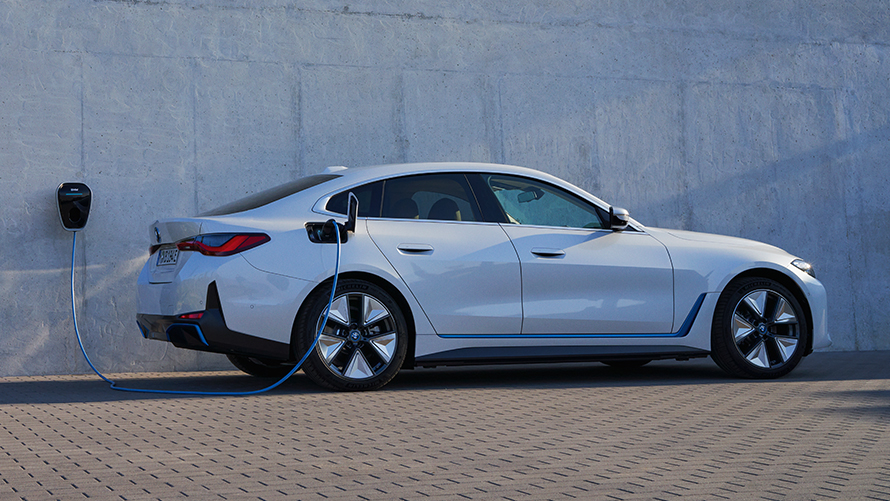 Imagine din partea laterală cu un sistem BMW Wallbox a unui BMW i4 eDrive40 G26 2021 Imagine din partea laterală a unui BMW i4 eDrive40 G26 2021 Alb Mineral în faţa peretelui unei case pe care este montată o staţie de încărcare BMW Wallbox