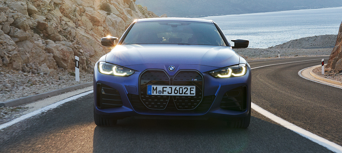 Imagine din partea frontală a unui BMW i4 M50 G26 2021 care se deplasează Imagine din partea frontală a unui BMW i4 M50 G26 2021 Albastru Portimao M care se deplasează pe şosea