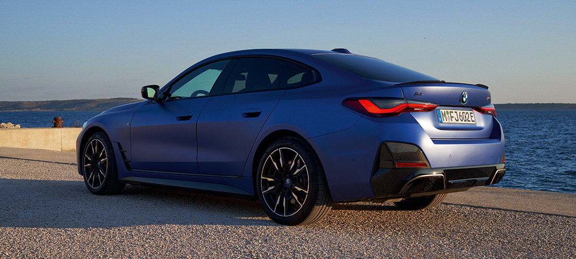 Imagine cu trei sferturi din partea din spate a unui BMW i4 M50 G26 2021 Imagine cu trei sferturi din partea din spate a unui BMW i4 M50 G26 2021 Albastru Portimao M care staţionează lângă un chei