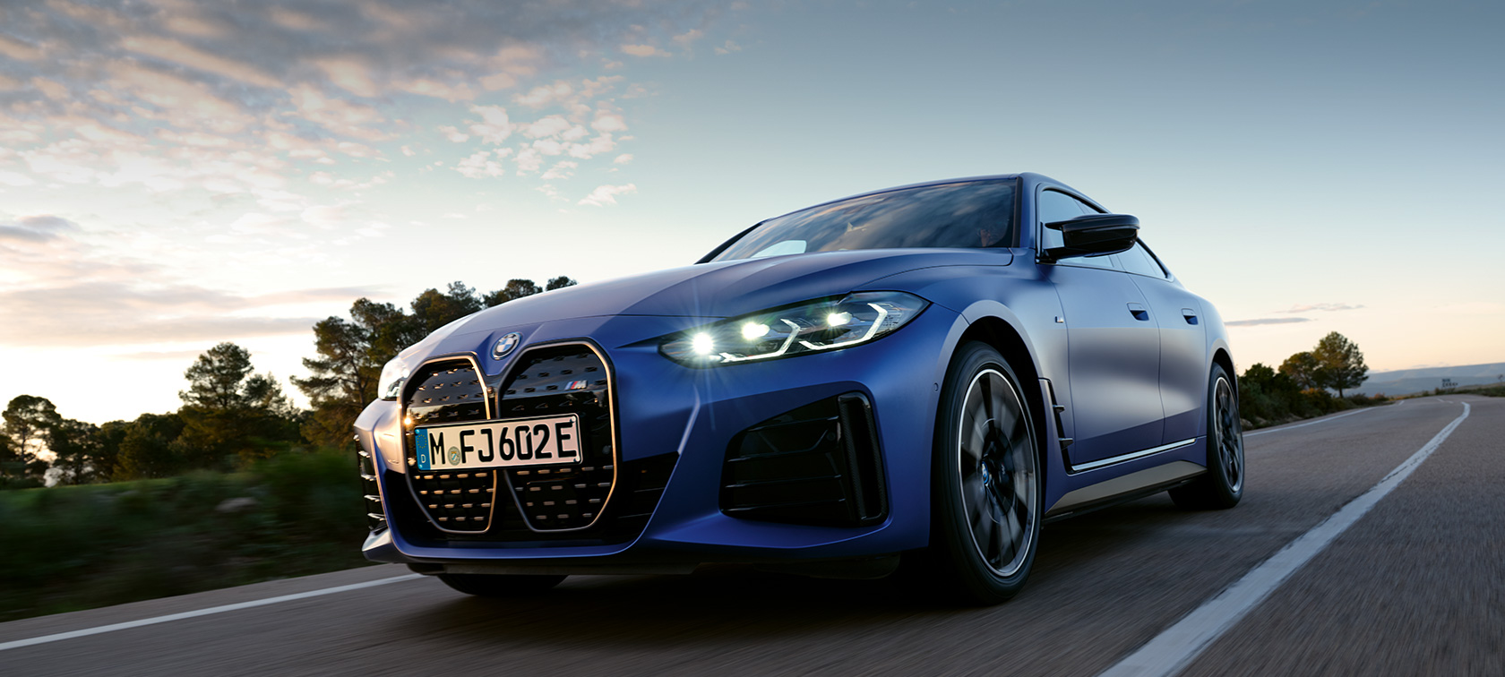 Imagine din partea laterală a unui BMW i4 M50 G26 2021 staţionând în faţa unui relief pietros Imagine din partea laterală a unui BMW i4 M50 G26 2021 BMW Individual Albastru Frozen Portimao staţionând în faţa unui relief pietros
