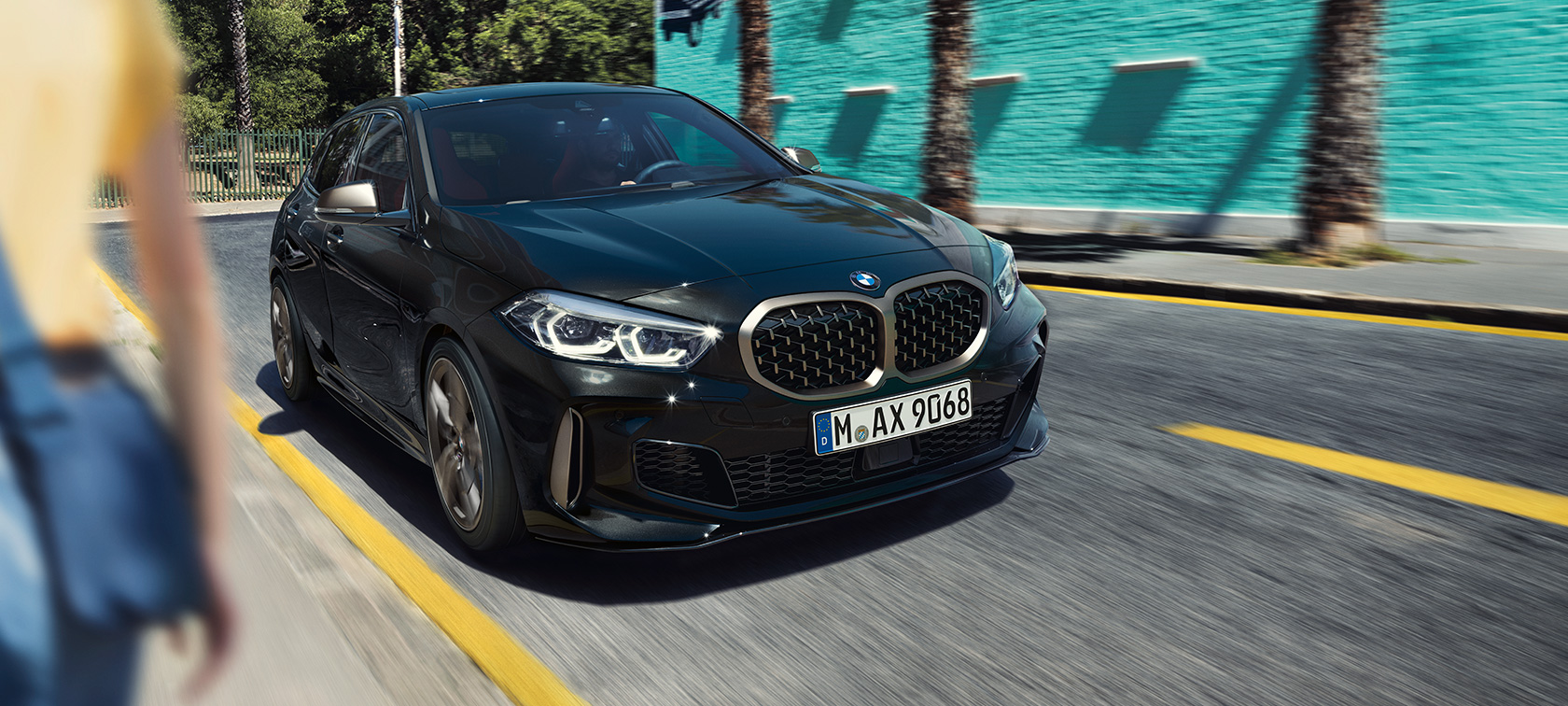 Imagine cu trei sferturi din partea frontală a BMW M135i xDrive. Imagine cu trei sferturi din partea frontală a BMW M135i xDrive în Negru Sapphire metalizat, rulând.