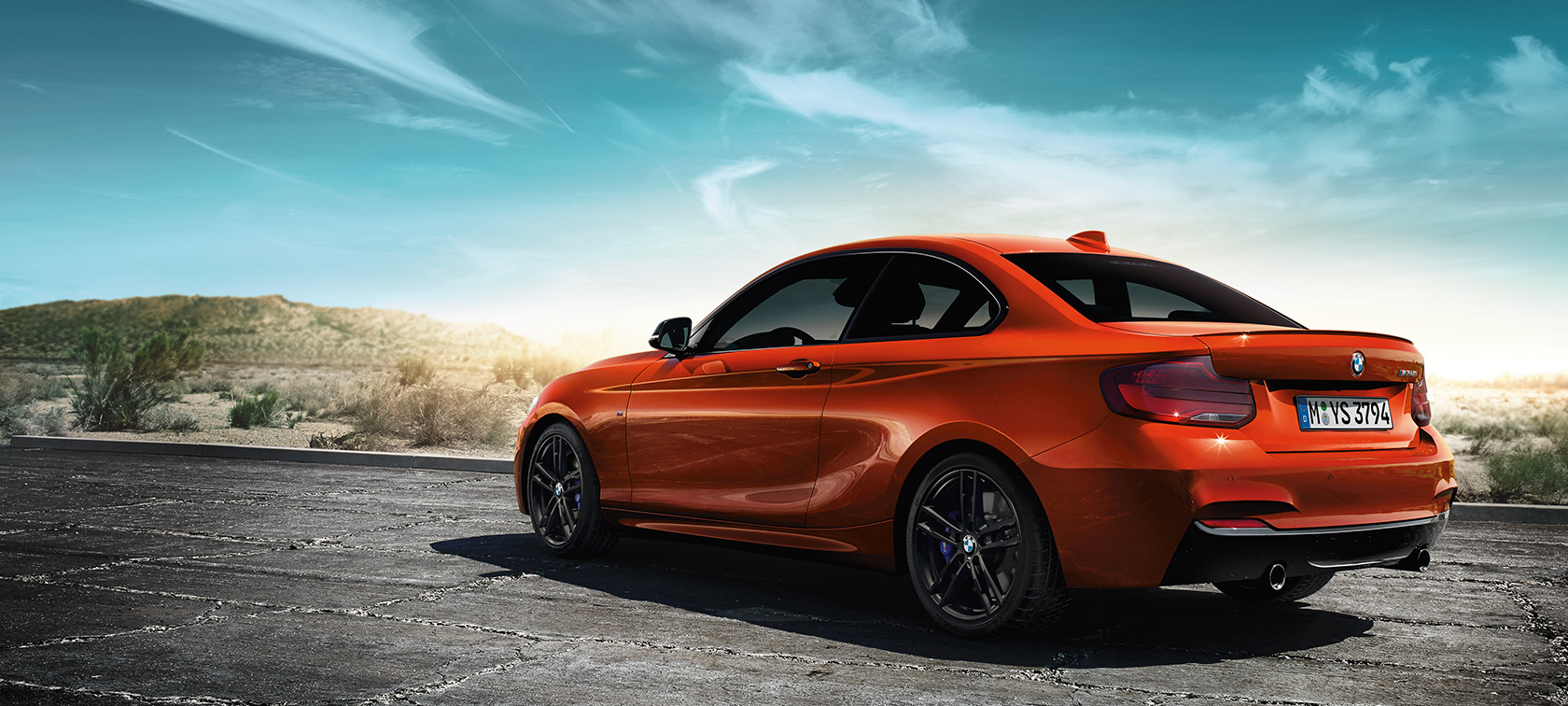 Imagine cu trei sferturi din partea din spate a BMW M240i Coupé F22 2017 Imagine cu trei sferturi din partea din spate a BMW M240i Coupé F22 2017, Portocaliu Sunset, staţionând în faţa peisajului de stepă