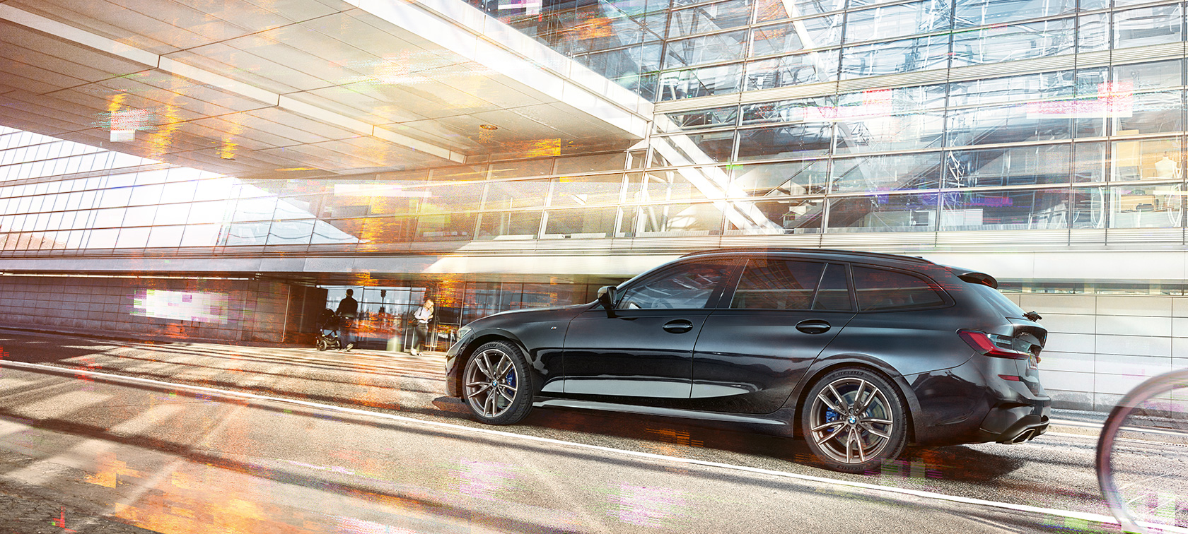 Perspectivă laterală a BMW M340i xDrive Touring, rulând Perspectivă laterală a BMW M340i xDrive Touring, rulând în faţa unei clădiri din sticlă
