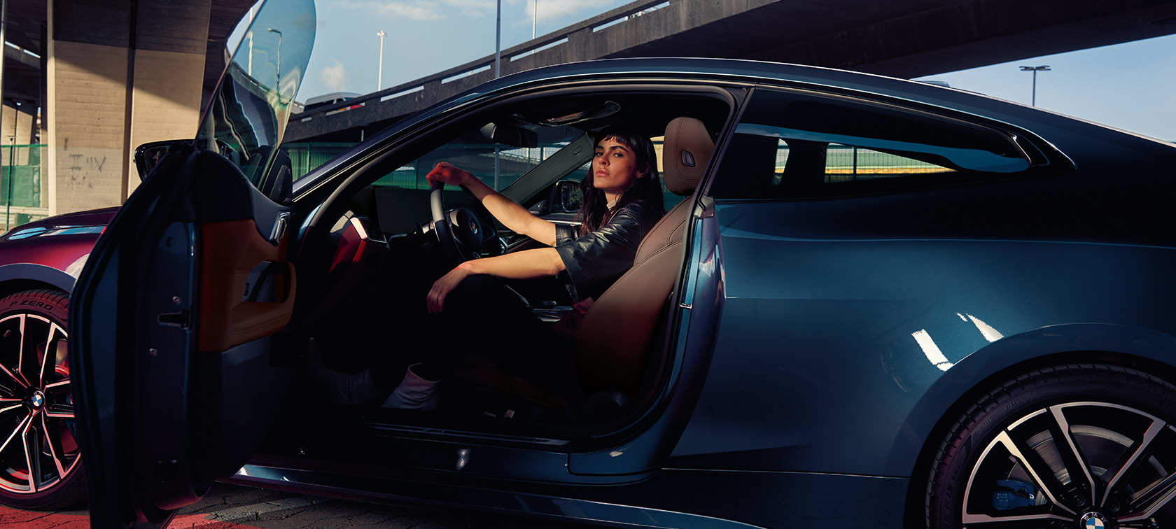 Imagine cu partea laterală a BMW M440i xDrive Coupé G22 2020, cu un model stând în automobil, cu portiera deschisă Imagine cu partea laterală a BMW M440i xDrive Coupé G22 2020 în Albastru Arctic Race metalizat, cu un model stând în automobil, cu portiera deschisă