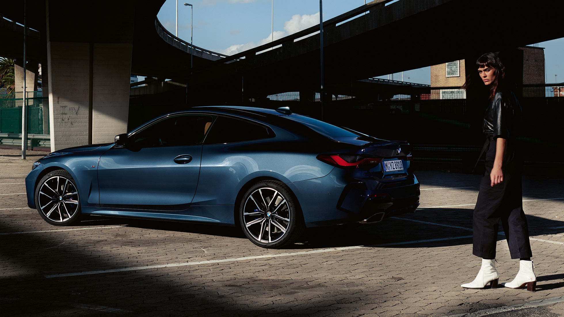 Imagine cu trei sferturi din partea spate a BMW M440i xDrive Coupé, G22, 2020, cu un model Imagine cu trei sferturi din partea spate a BMW M440i xDrive Coupé, G22, 2020, în Albastru Arctic Race metalizat, cu un model