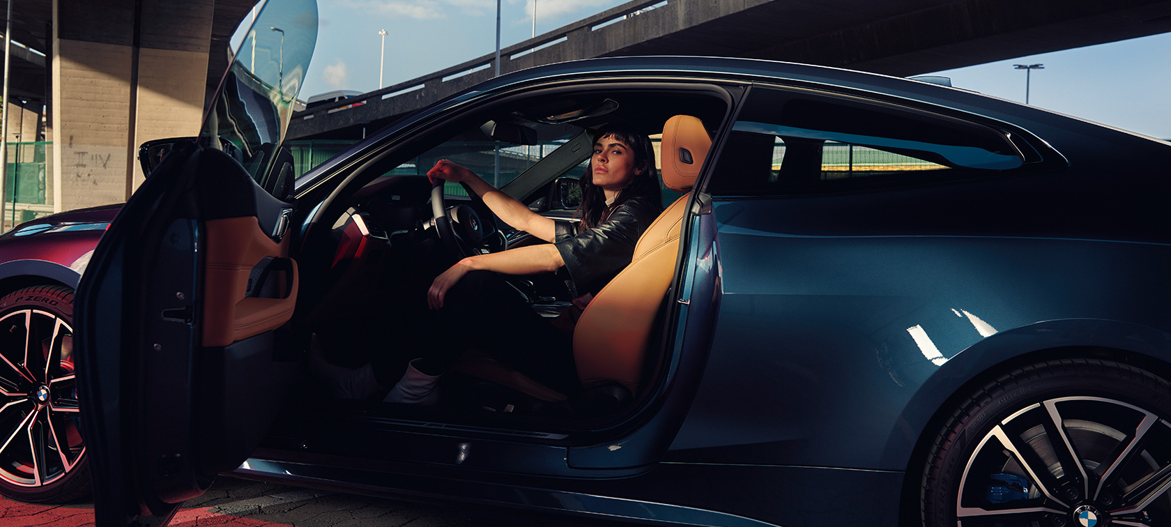 Imagine cu partea laterală a BMW M440i xDrive Coupé, G22, 2020, cu un model Imagine cu partea laterală a BMW M440i xDrive Coupé, G22, 2020, în Albastru Arctic Race metalizat, cu un model stând în automobil, cu portiera deschisă