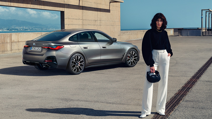 Imagine cu trei sferturi din partea din spate a BMW M440i xDrive Gran Coupé G26 2021, cu un model Imagine cu trei sferturi din partea din spate a modelului BMW M440i xDrive Gran Coupé G26 2021, în Gri Frozen Pure, cu un model