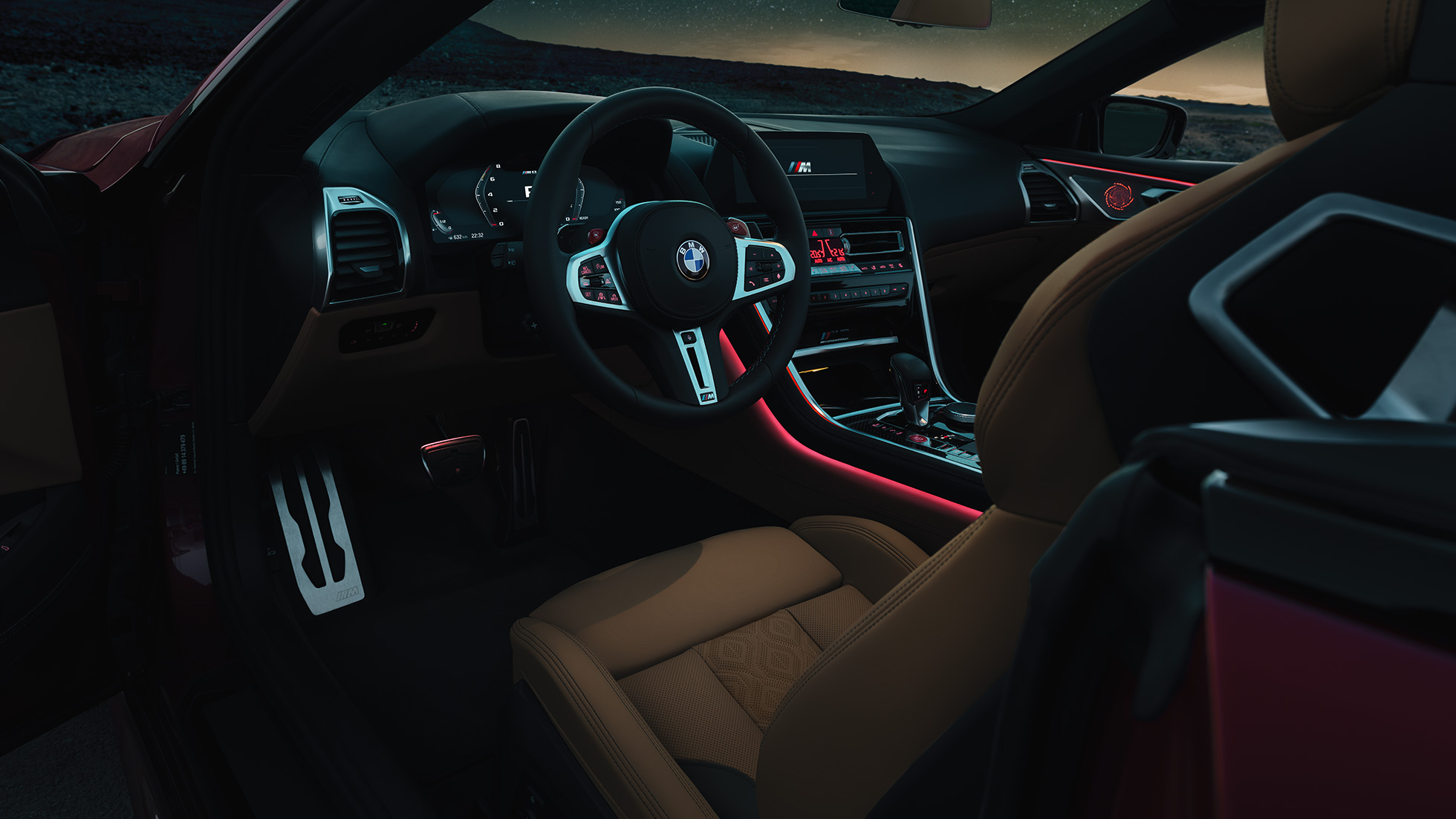 Habitaclul BMW M8 Competition Cabriolet. Habitaclul BMW M8 Cabriolet cu volan sport îmbrăcat în piele şi iluminare ambientală roşie, pe timp de noapte.