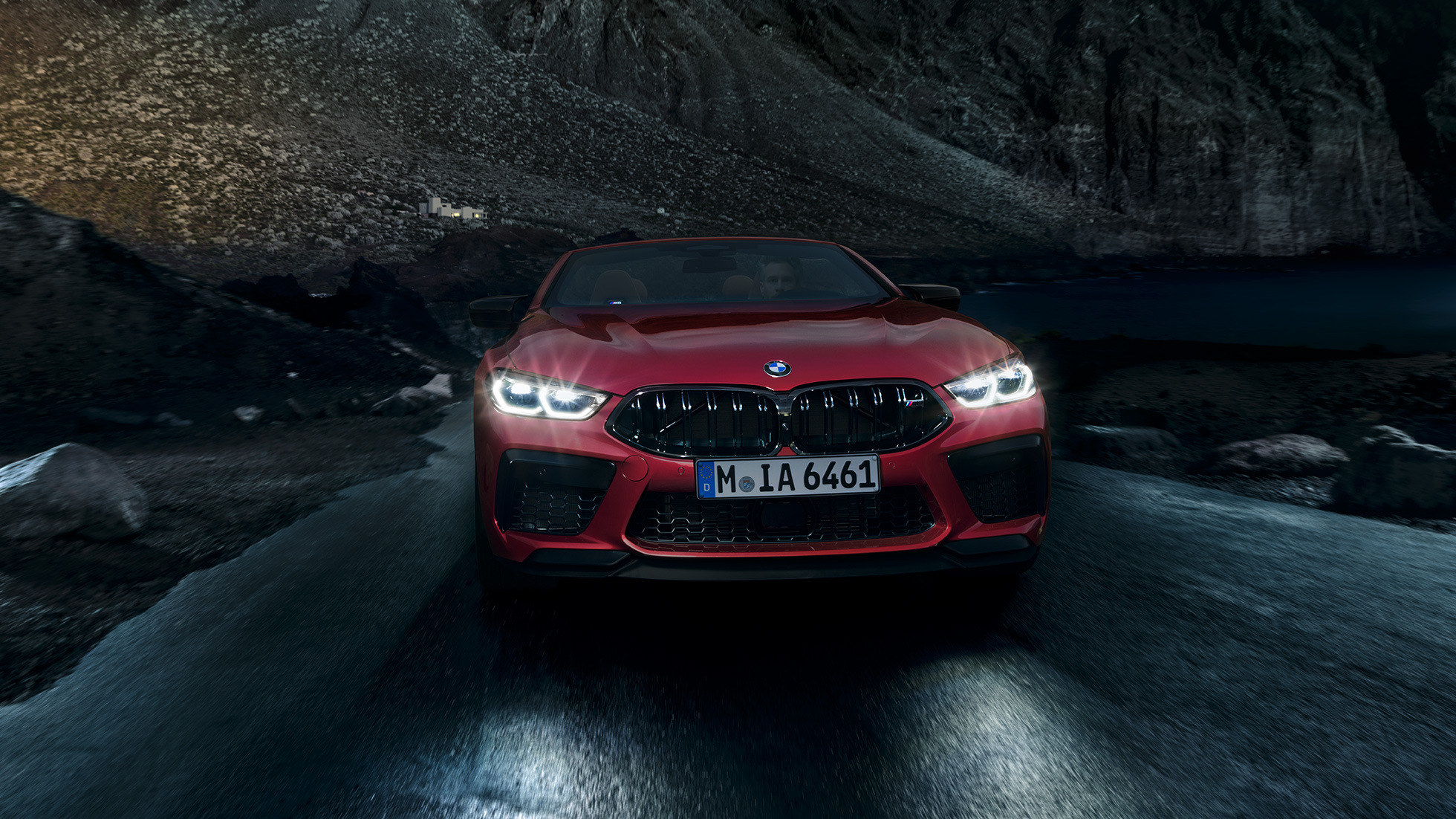 Imagine cu partea frontală a BMW M8 Competition Cabriolet. Imagine cu partea frontală a BMW M8 Competition Cabriolet în Roşu Motegi metalizat, cu faruri strălucitoare, rulând noaptea.