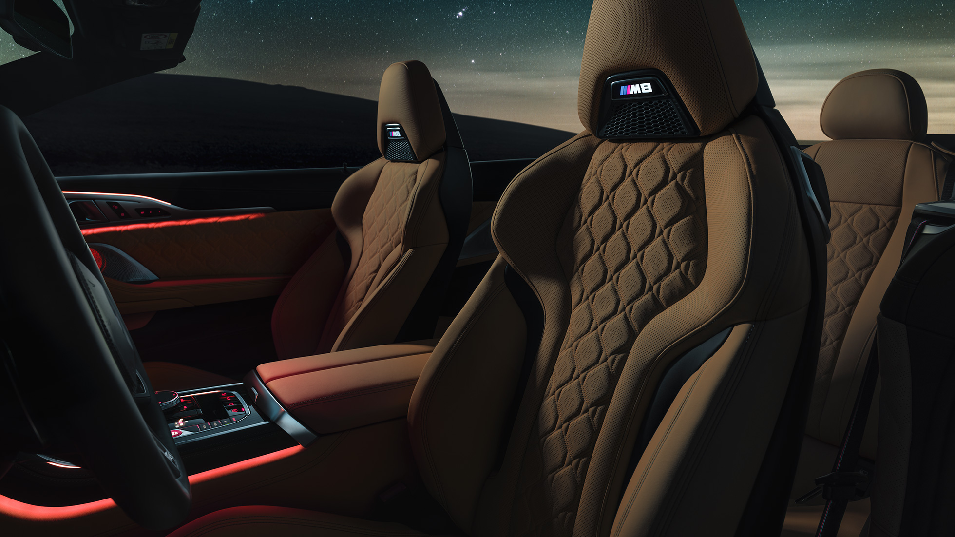 Scaune M Sport din piele Merino. Interiorul BMW M8 Cabriolet cu soft-top-ul deschis, cu scaune M Sport din piele Merino şi iuminare ambientală roşie, sub cerul înstelat.
