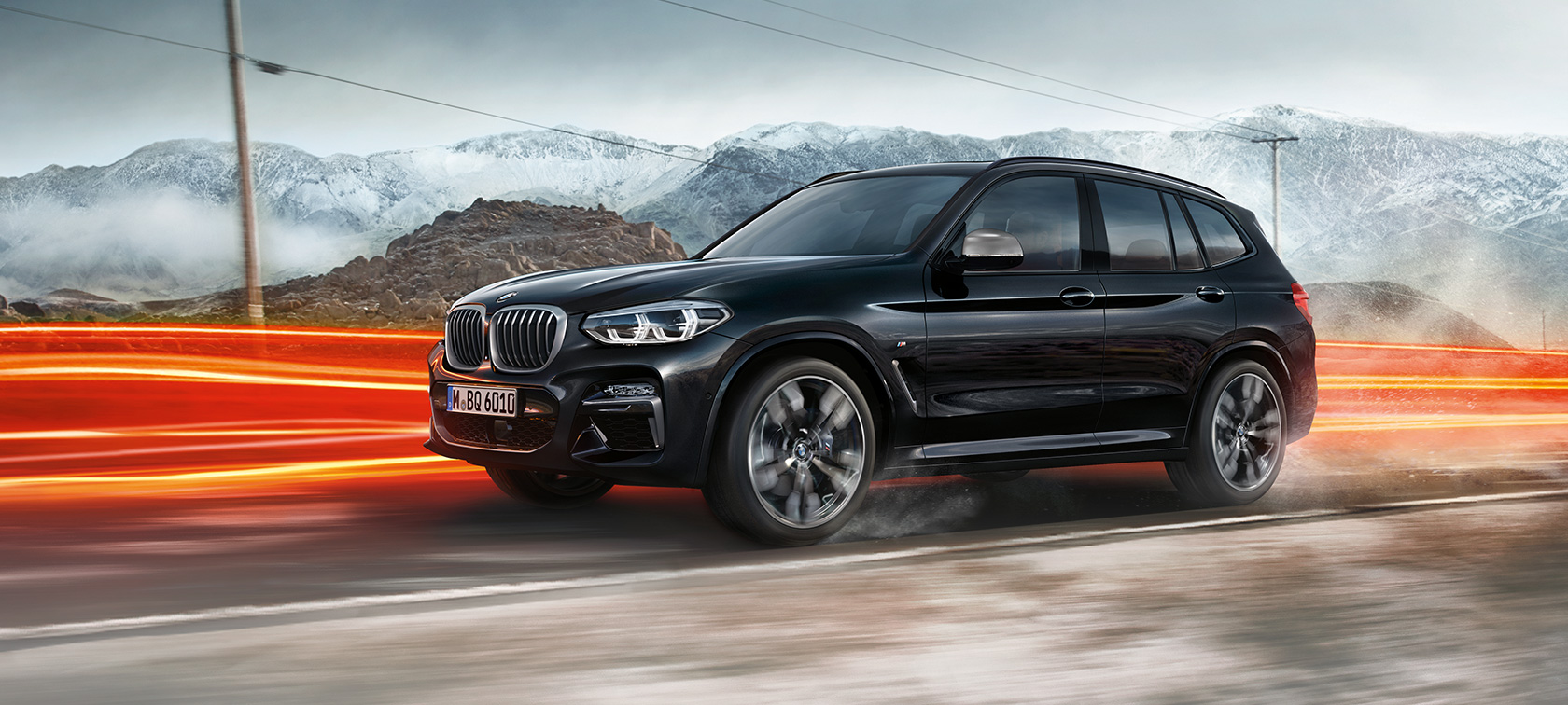 Perspectivă laterală a BMW X3 M40i şi BMW X3 M40d. Perspectivă laterală exterioară a BMW X3 M40i şi BMW X3 M40d în Negru Sapphire metalizat în faţa unui peisaj montan cu raze de lumină.