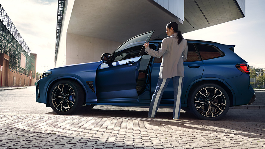 Imagine din partea laterală a unui BMW X3 M Competition F97 LCI 2021, cu portiera deschisă şi model feminin Imagine din partea laterală a unui BMW X3 M Competition F97 LCI Facelift 2021 în Albastru Frozen Marina Bay, cu portiera deschisă şi model feminin