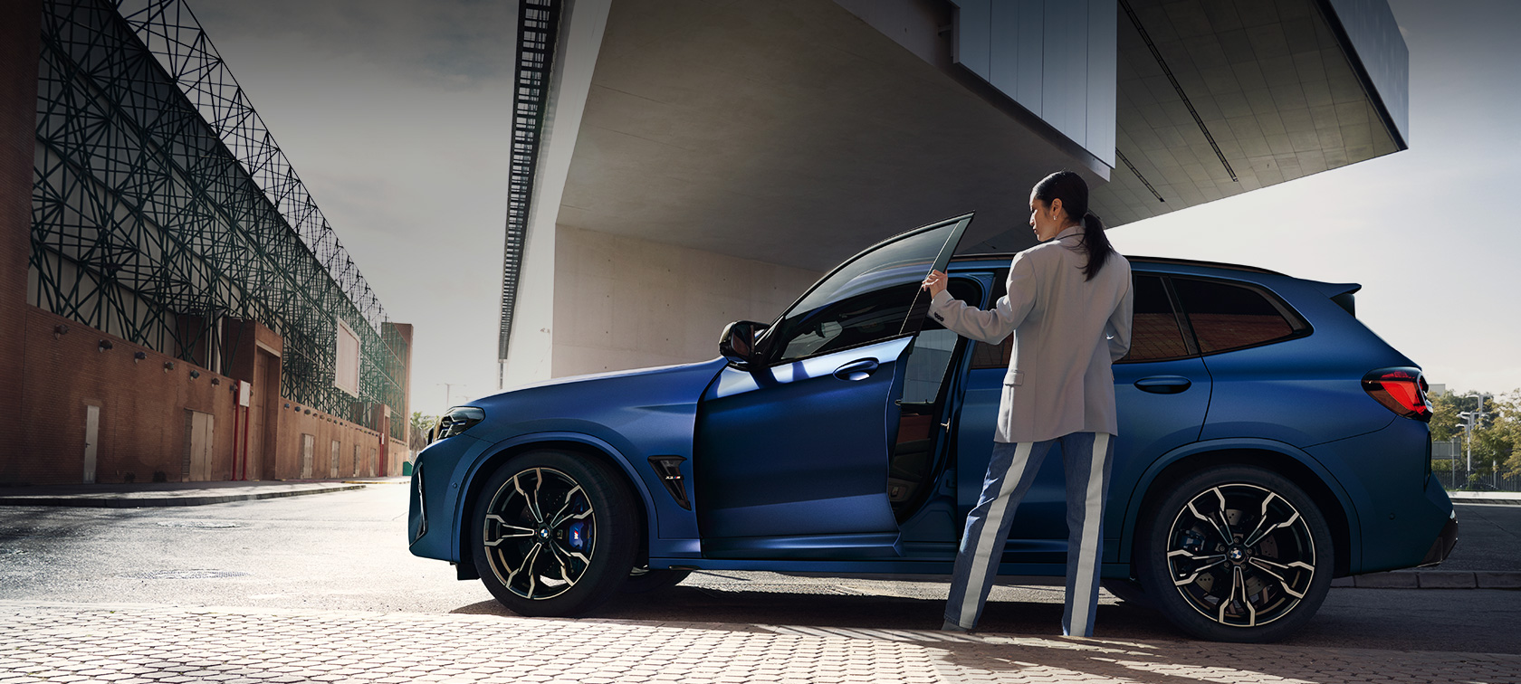 Imagine din partea laterală cu un BMW X3 M Competition F97 LCI Facelift 2021, staţionând Imagine din partea laterală a unui BMW X3 M Competition F97 LCI Facelift 2021 în BMW Individual Albastru Frozen Portimao, staţionând cu portiera deschisă şi model feminin