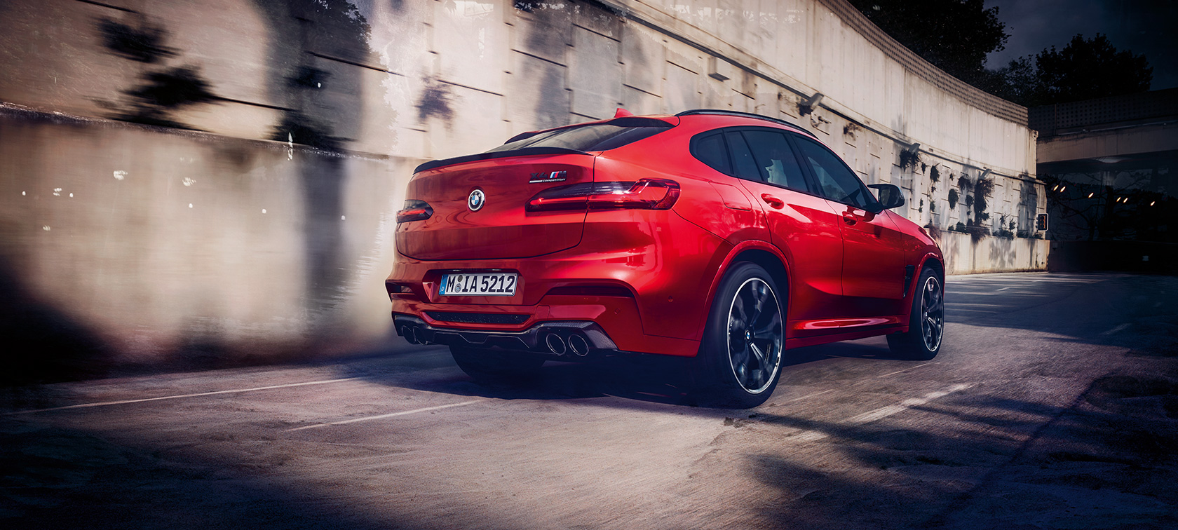 Imagine cu trei sferturi din partea spate a BMW X4 M Competition. Imagine cu trei sferturi din partea spate exterioară a BMW X4 M Competition în Roşu Toronto metalizat rulând.