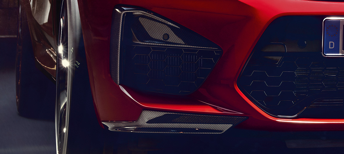 BMW X4 M Competition, cu inserţii ale elementelor laterale ale spoilerelor şi grile de aer din carbon. Imagine cu exteriorul BMW X4 M Competition în Roşu Toronto metalizat, cu pachet M din carbon pentru exterior, cu inserţii ale elementelor laterale ale spoilerelor şi grile de aer din carbon.