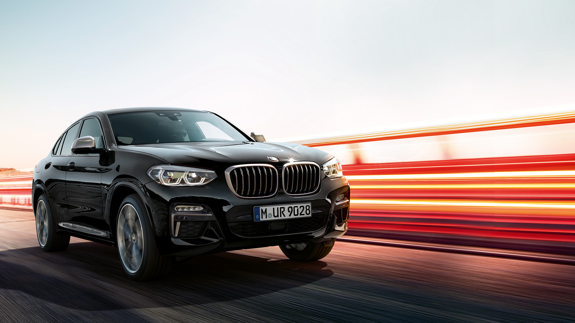 Imagine cu trei sferturi din partea spate a BMW X4 M40i. Imagine cu trei sferturi din partea spate exterioară a BMW X4 M40i în Negru Sapphire metalizat cu raze de lumină.