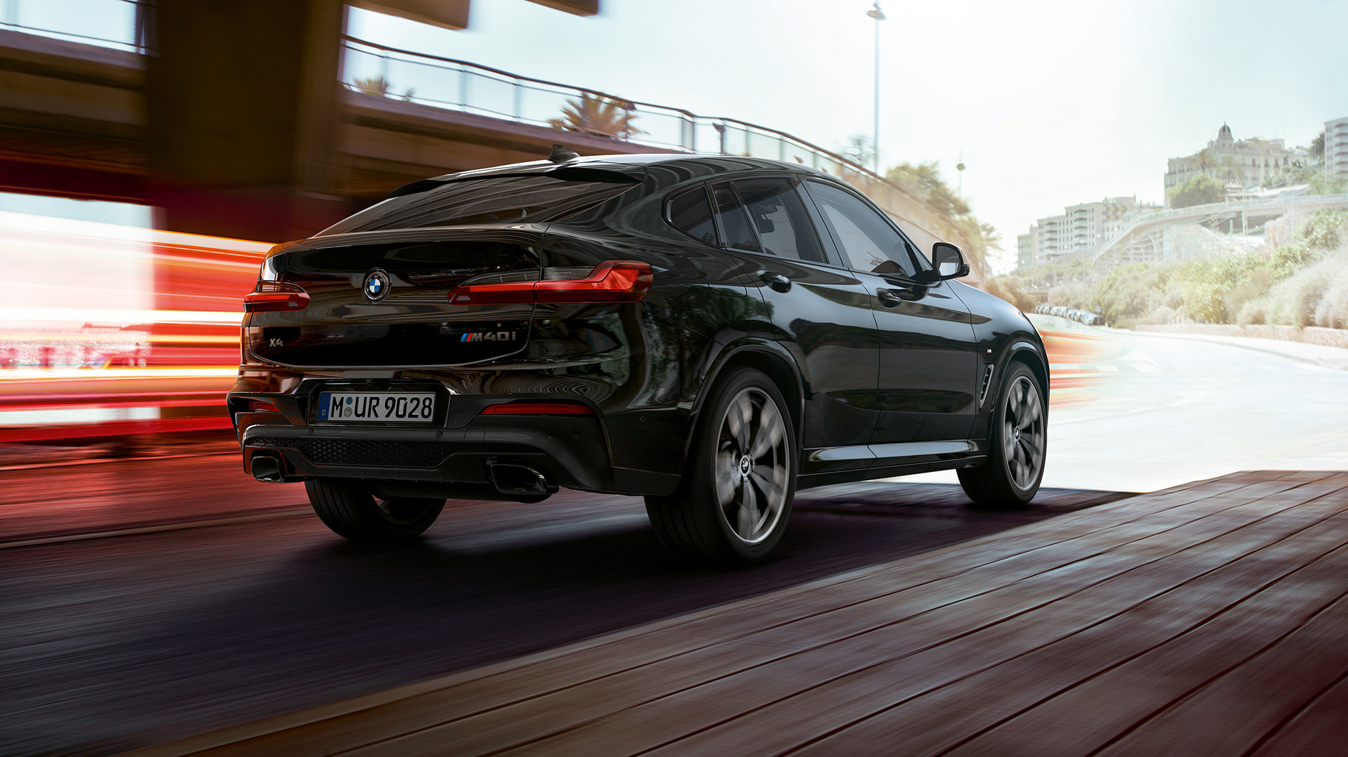Imagine cu trei sferturi din partea spate a BMW X4 M40i. Imagine cu trei sferturi din partea spate dreaptă a BMW X4 M40i în Negru Sapphire metalizat cu raze de lumină.