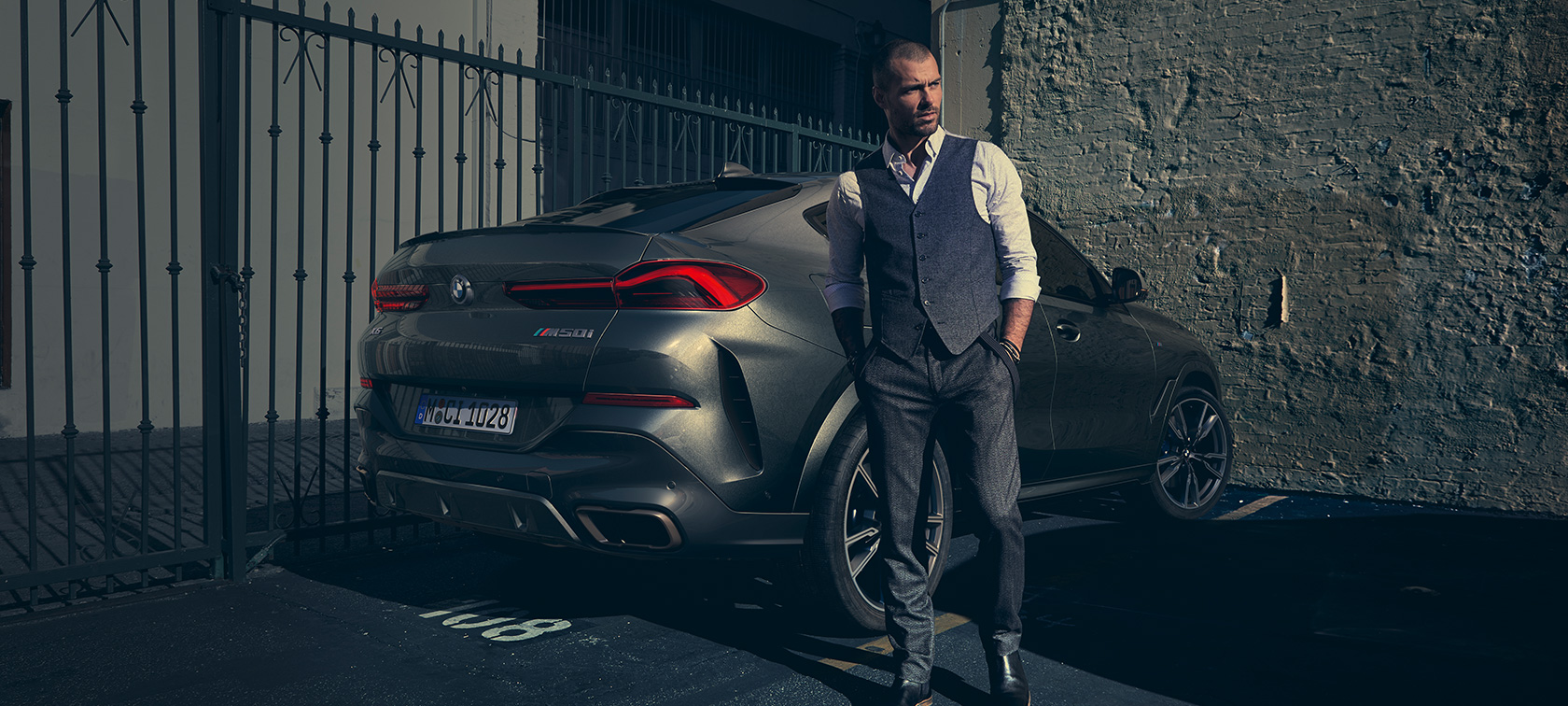 Imagine cu trei sferturi din partea din spate a BMW X6 M50i Imagine cu trei sferturi din partea din spate a BMW X6 M50i SUV, cu un bărbat lângă