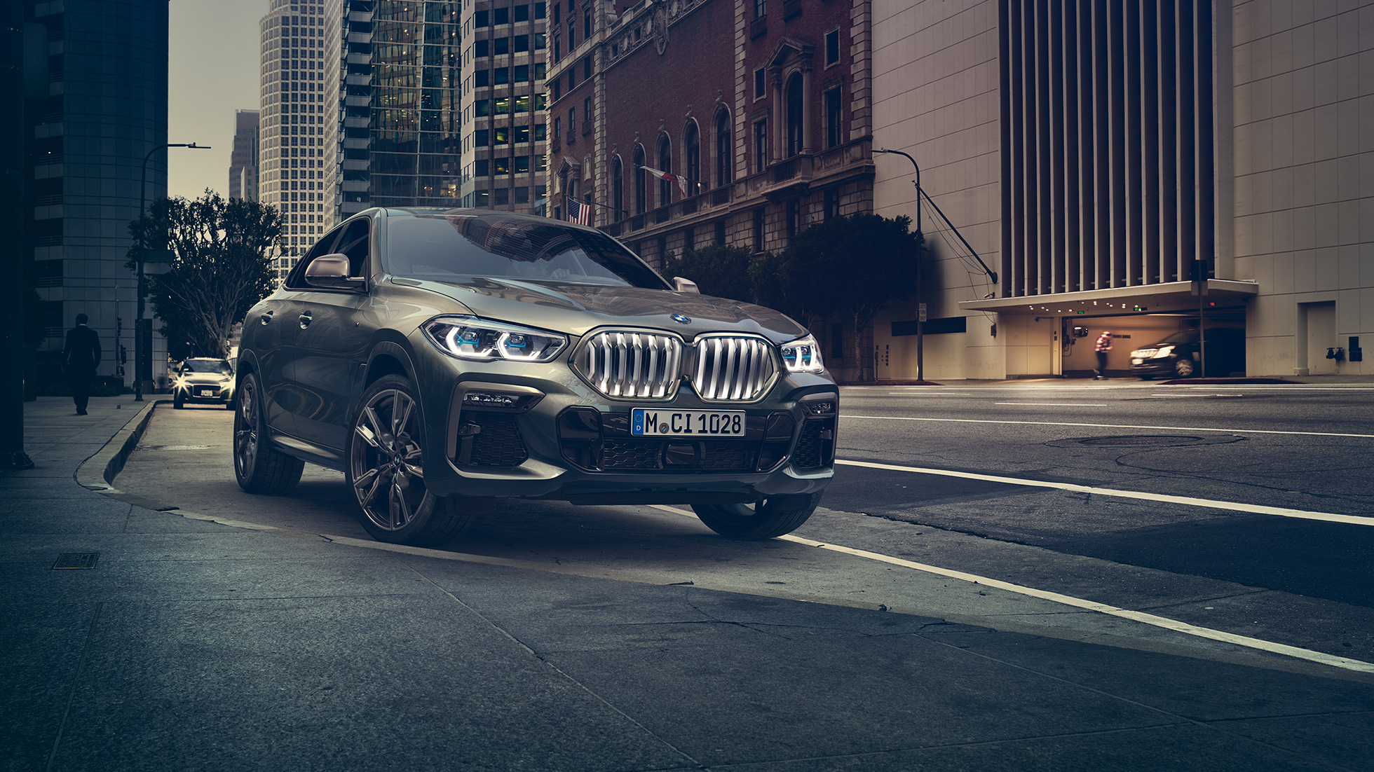 BMW X6 M50i staţionând Imagine cu trei sferturi din perspectivă frontală a BMW X6 M50i, staţionând în faţa unui peisaj urban