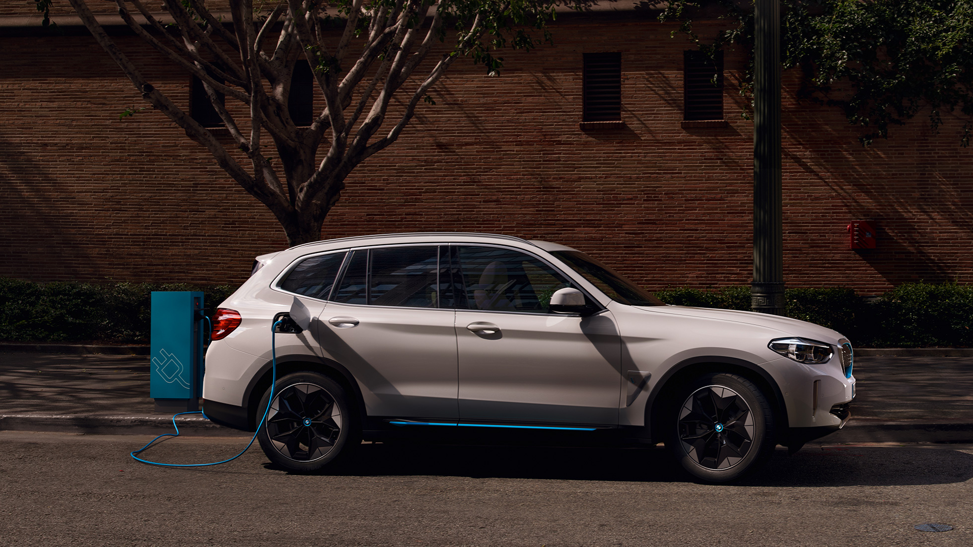 Imagine din lateral cu BMW iX3, G08, la o staţie publică cu putere mare de încărcare Imagine din lateral cu BMW iX3, G08, 2020, în Alb Mineral metalizat, la o staţie publică cu putere mare de încărcare