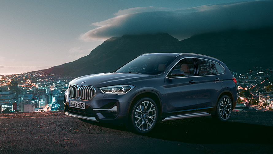 Imagine cu trei sferturi din partea laterală a BMW X1 F48 din a doua generaţie staţionând în faţa unui oraş Imagine cu trei sferturi din partea laterală a BMW Seria X BMW X1 F48 din a doua generaţie staţionând în faţa unui oraş