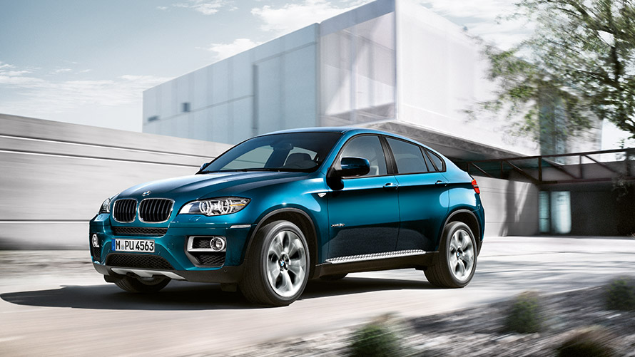 Imagine cu trei sferturi din partea laterală a BMW X6 E71 din prima generaţie staţionând în faţa unei clădiri Imagine cu trei sferturi din partea laterală a BMW Seria X BMW X6 E71 din prima generaţie staţionând în faţa unei clădiri