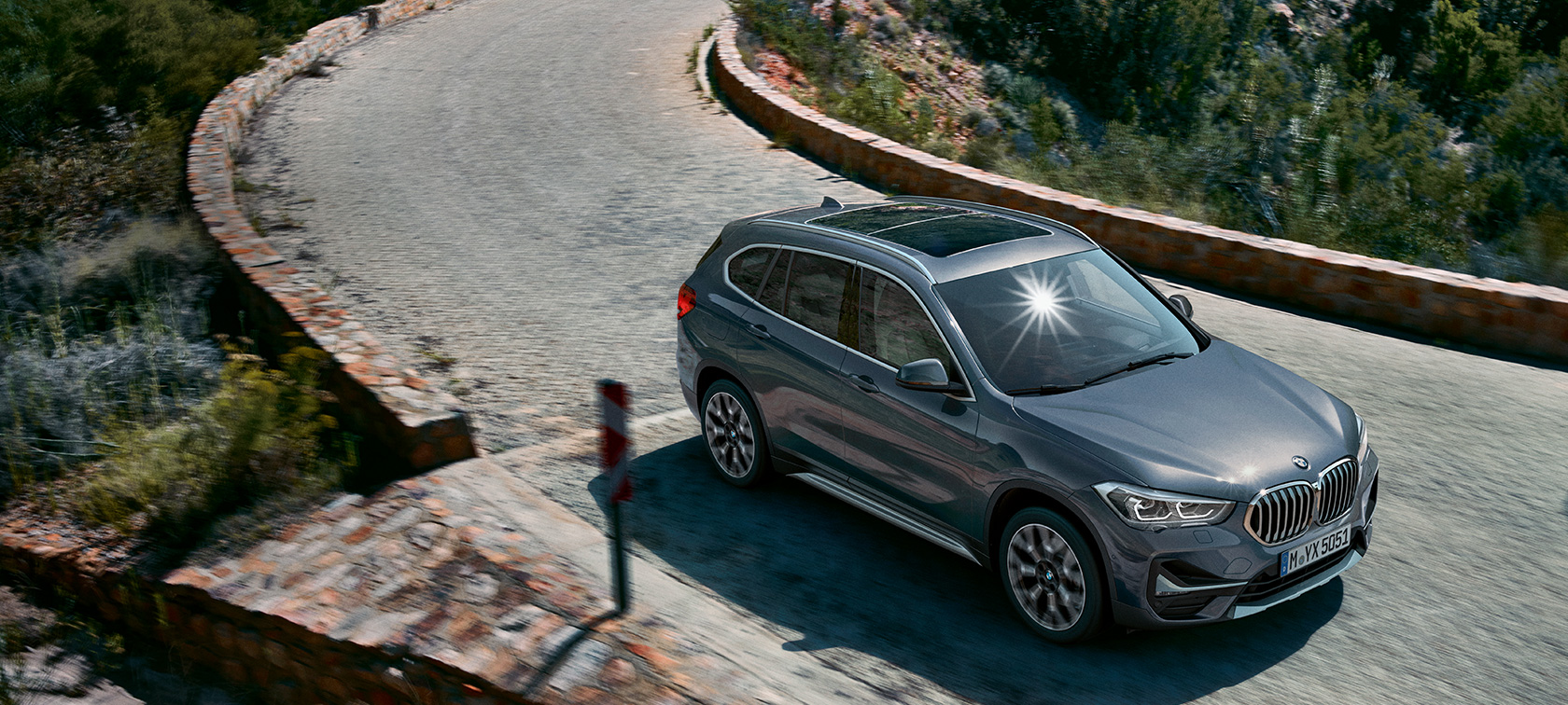 Imagine cu trei sferturi din partea frontală a BMW X1. Imagine cu trei sferturi din partea frontală a BMW X1 rulând într-un peisaj montan.