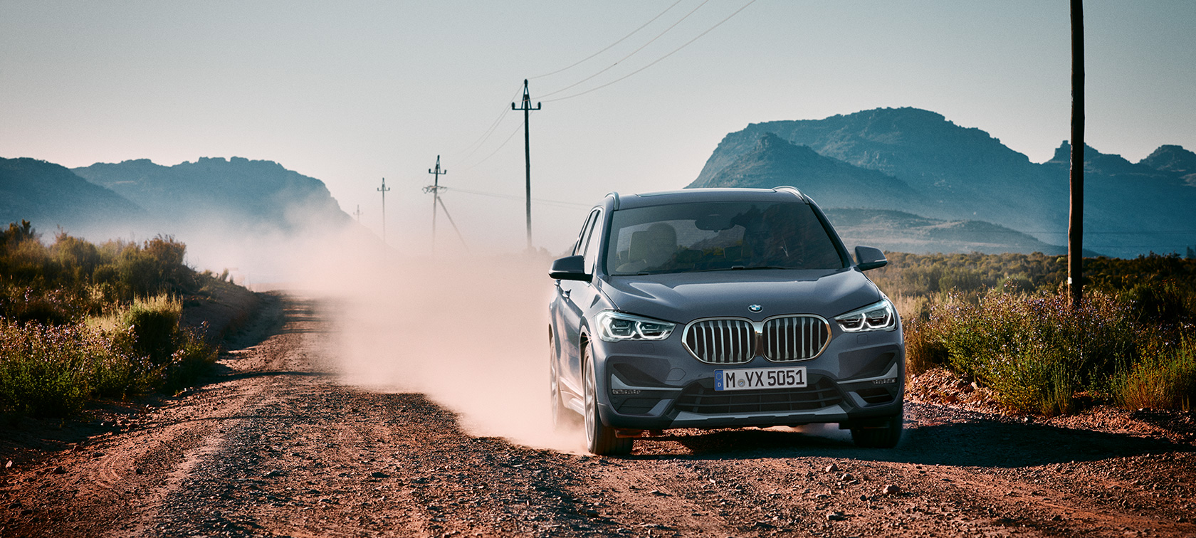 Imagine cu trei sferturi din partea spate a BMW X1. Imagine cu trei sferturi din partea spate a BMW X1 rulând într-un peisaj montan.