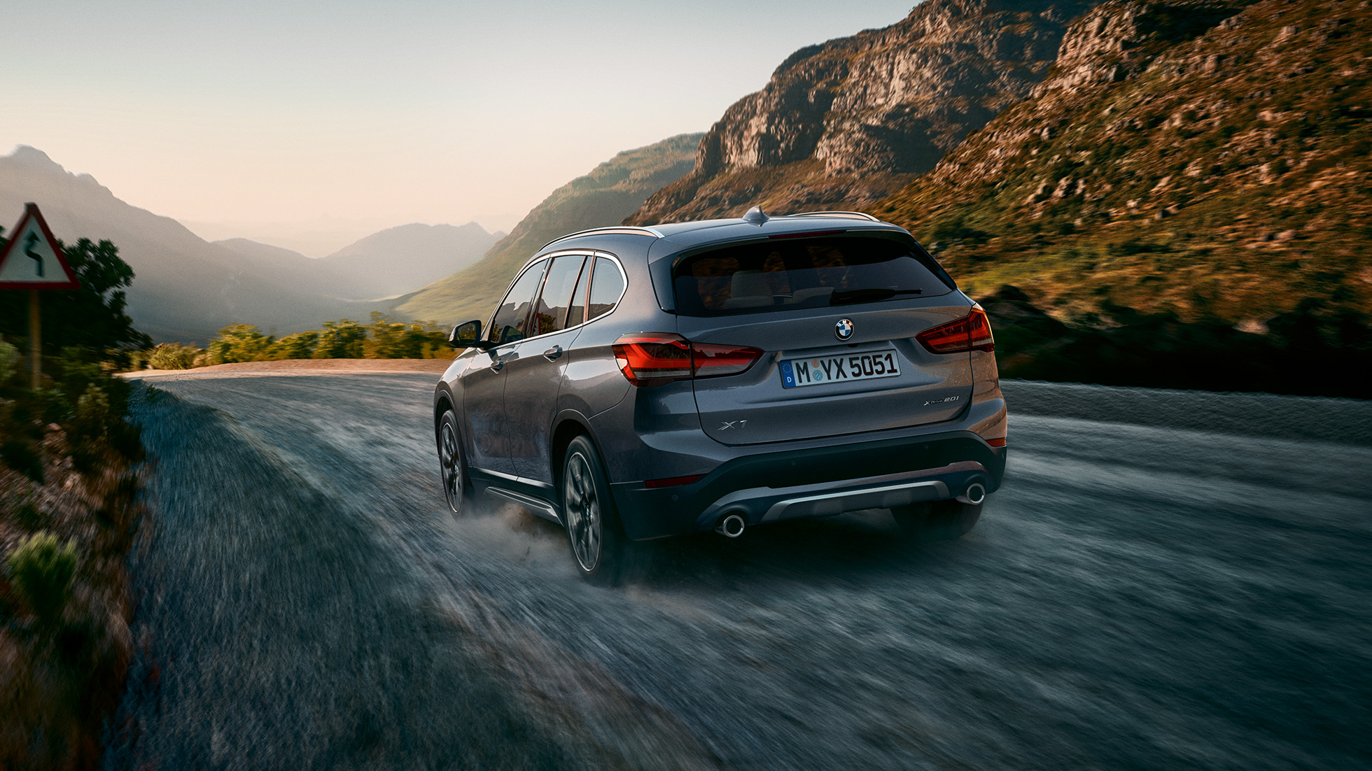 Imagine cu trei sferturi din partea spate a BMW X1. Imagine cu trei sferturi din partea spate a BMW X1 rulând într-un peisaj montan.