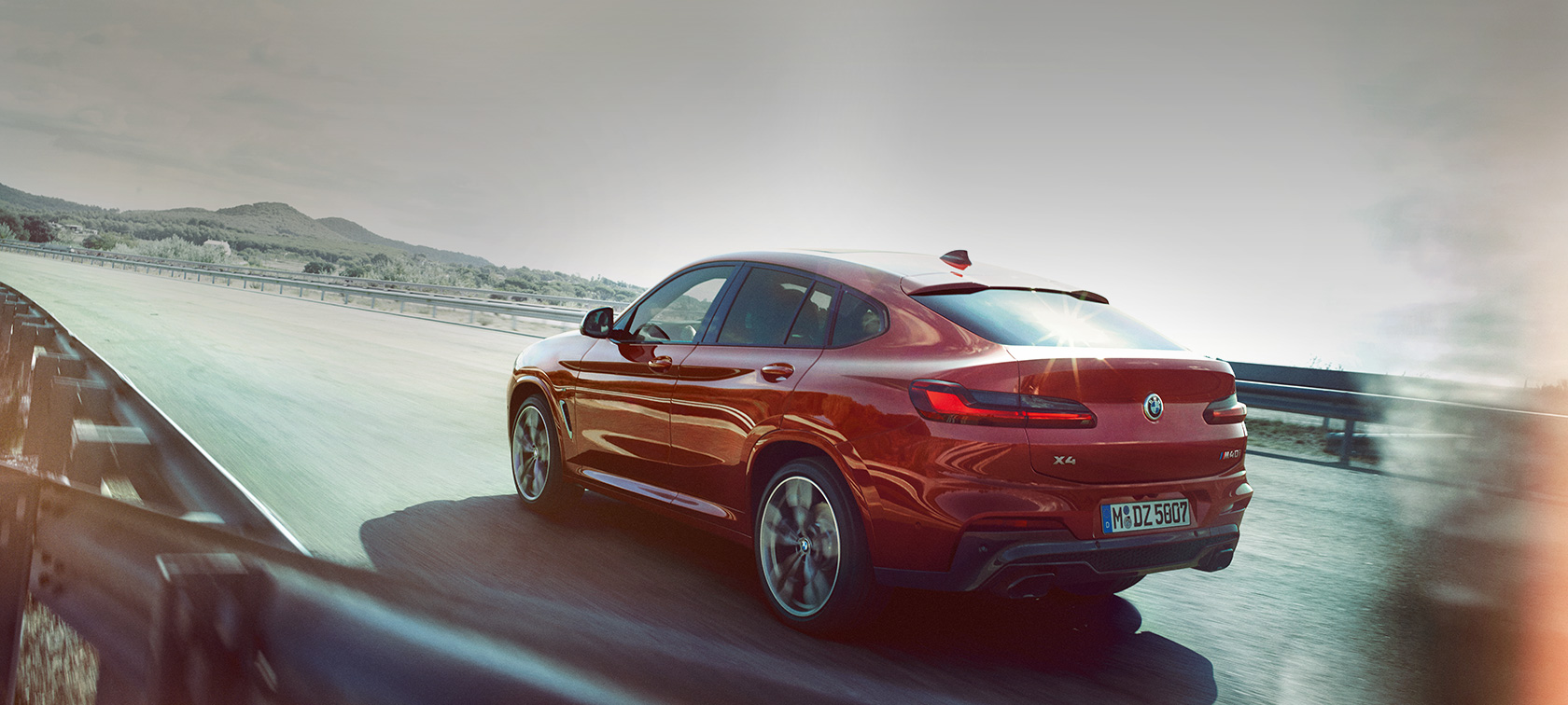 BMW X4 rulând pe drum Imagine cu trei sferturi din partea spate a BMW X4 M40i, G02, 2018, în Roşu Flamenco Brilliant Effect, rulând pe drum